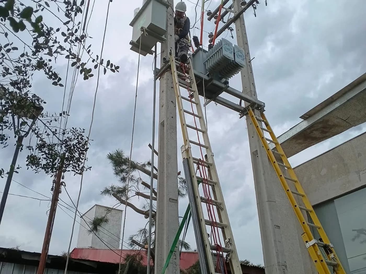 Técnico de A/Z con arnés trabajando en un poste de media tensión, junto a un transformador